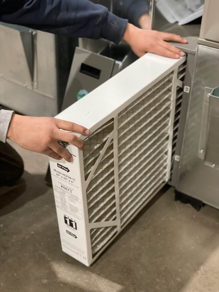 Hands replacing a pleated HVAC air filter.