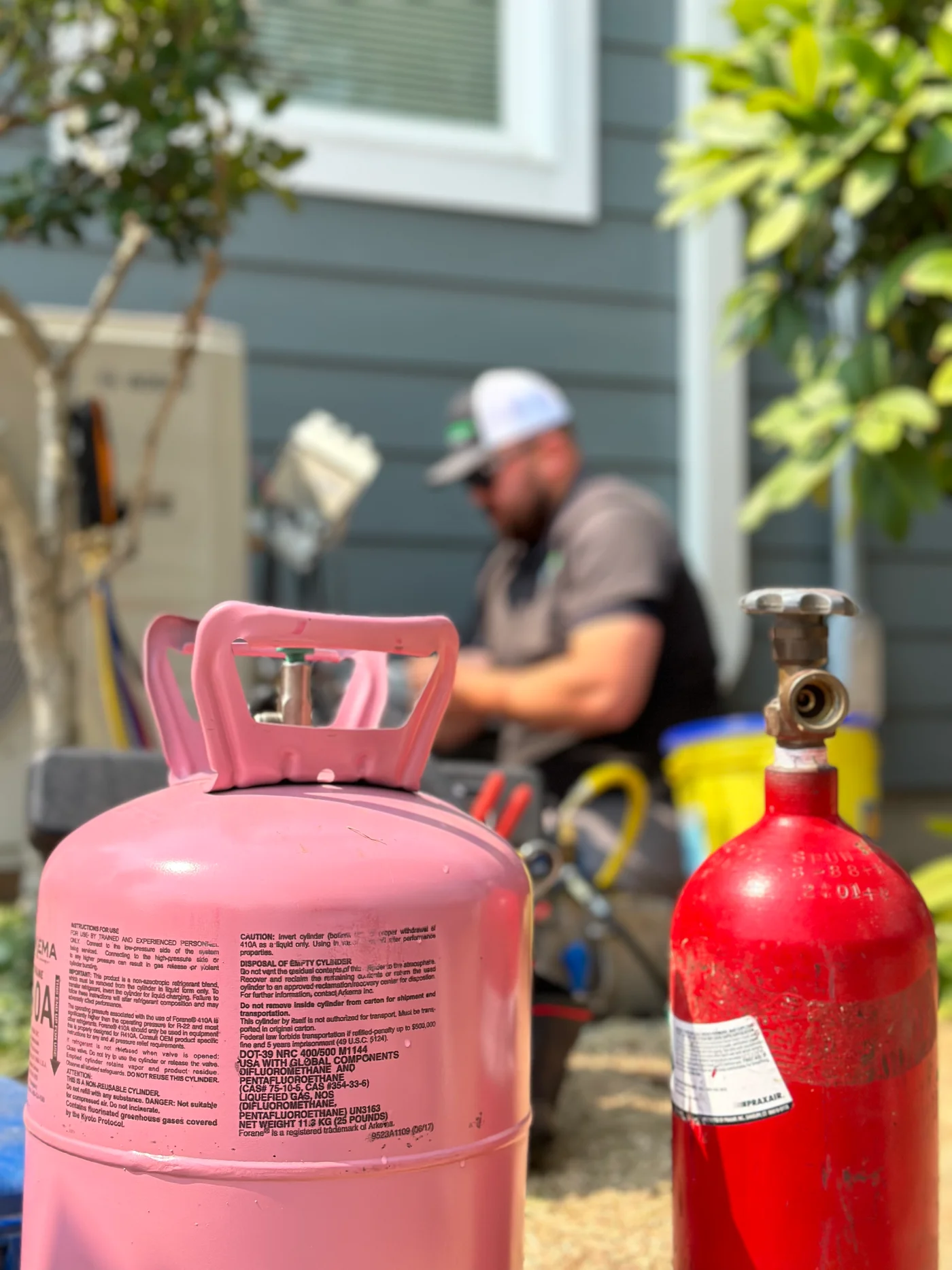 Tristin Morris of Oregon Climate Tech weighing in refrigerant on a Mitsubishi mini-split install, with a pink R-410A tank and red nitrogen tank visible in the foreground.